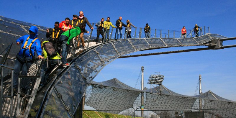 In über 50 Metern Höhe eröffnen sich atemberaubende Perspektiven: Der Blick schweift über die Stadtkulisse Münchens mit den Türmen der Frauenkirche. Bei gutem Wetter reicht die Sicht sogar bis zu den Alpen mit Deutschlands höchstem Berg, der Zugspitze. Eine Tour über das Zeltdach des Olympiastadions weckt die Begeisterung für die Architektur und Konstruktion des weltberühmten Stadions der XX. Olympischen Sommerspiele von 1972. At a height of over 50 metres, breathtaking perspectives open up: The view sweeps over the cityscape of Munich with the towers of the Frauenkirche. In good weather, the view even reaches as far as the Alps with Germany's highest mountain, the Zugspitze. A tour over the tent roof of the Olympic Stadium awakens enthusiasm for the architecture and construction of the world-famous stadium of the XX Summer Olympic Games of 1972.